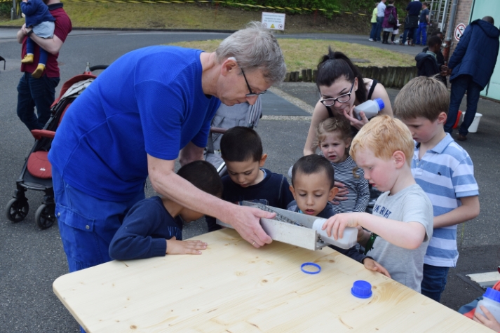 Kinder gießen Abwasser durch ein kleines Rechenmodell und lernen so, dass Grobstoffe zurückgehalten werden.